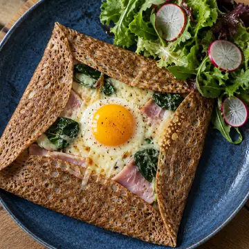 Buckwheat galette folded around a fried egg, ham, gruyère and spinach, with a radish salad